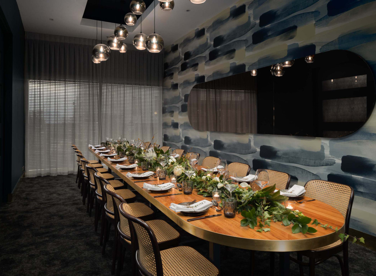 A modern private dining room at Rydges Auckland features a long, elegantly set table against a vibrant artistic wall.