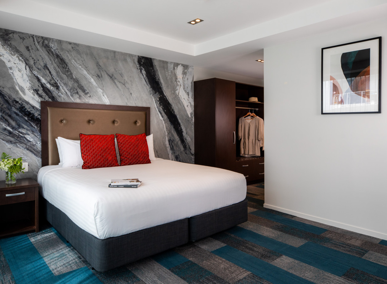 A modern hotel bedroom featuring a marble-effect accent wall and patterned carpet at the stylish Rydges Auckland.