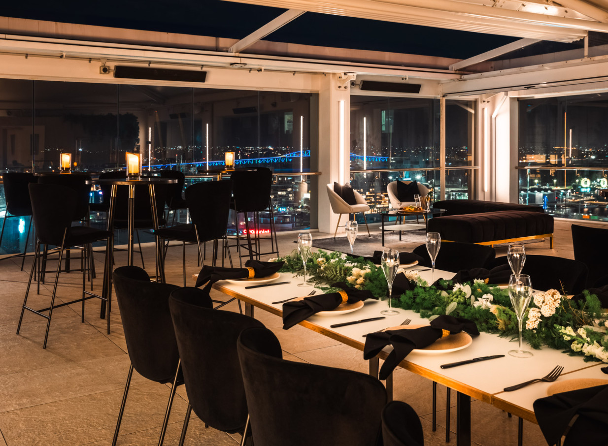 Rydges Auckland's chic rooftop terrace offers modern dining and lounge seating with panoramic city views.