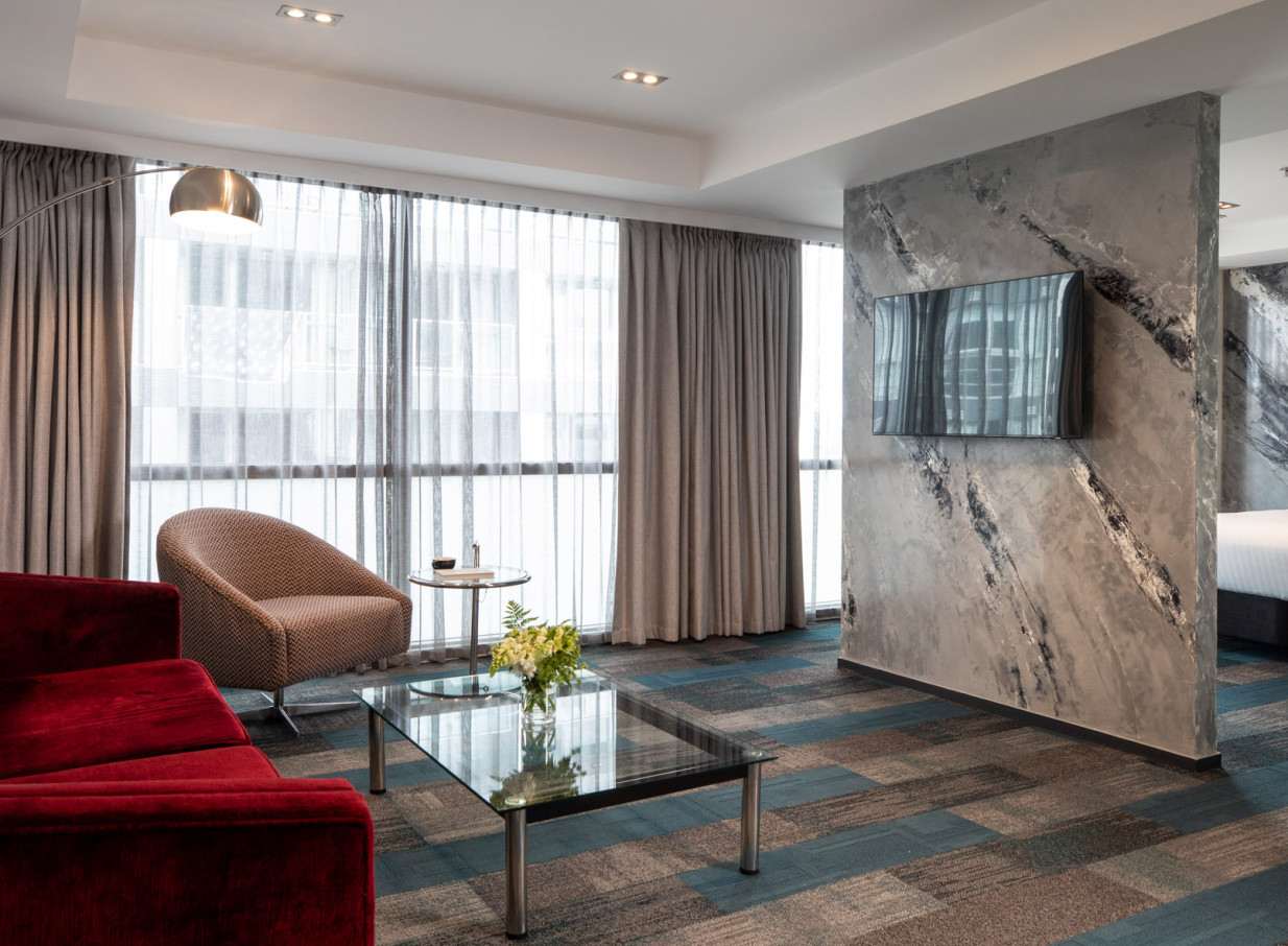 A contemporary living area with a red sofa, patterned chair, and a distinctive textured feature wall, reflecting the stylish design of Rydges Auckland.