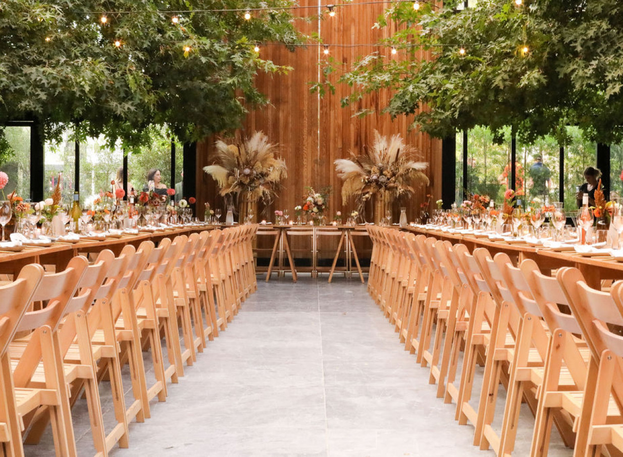 Glasshouse Morningside in Auckland offers an industrial-chic reception dining room featuring glass walls, indoor trees, and elegant place settings.