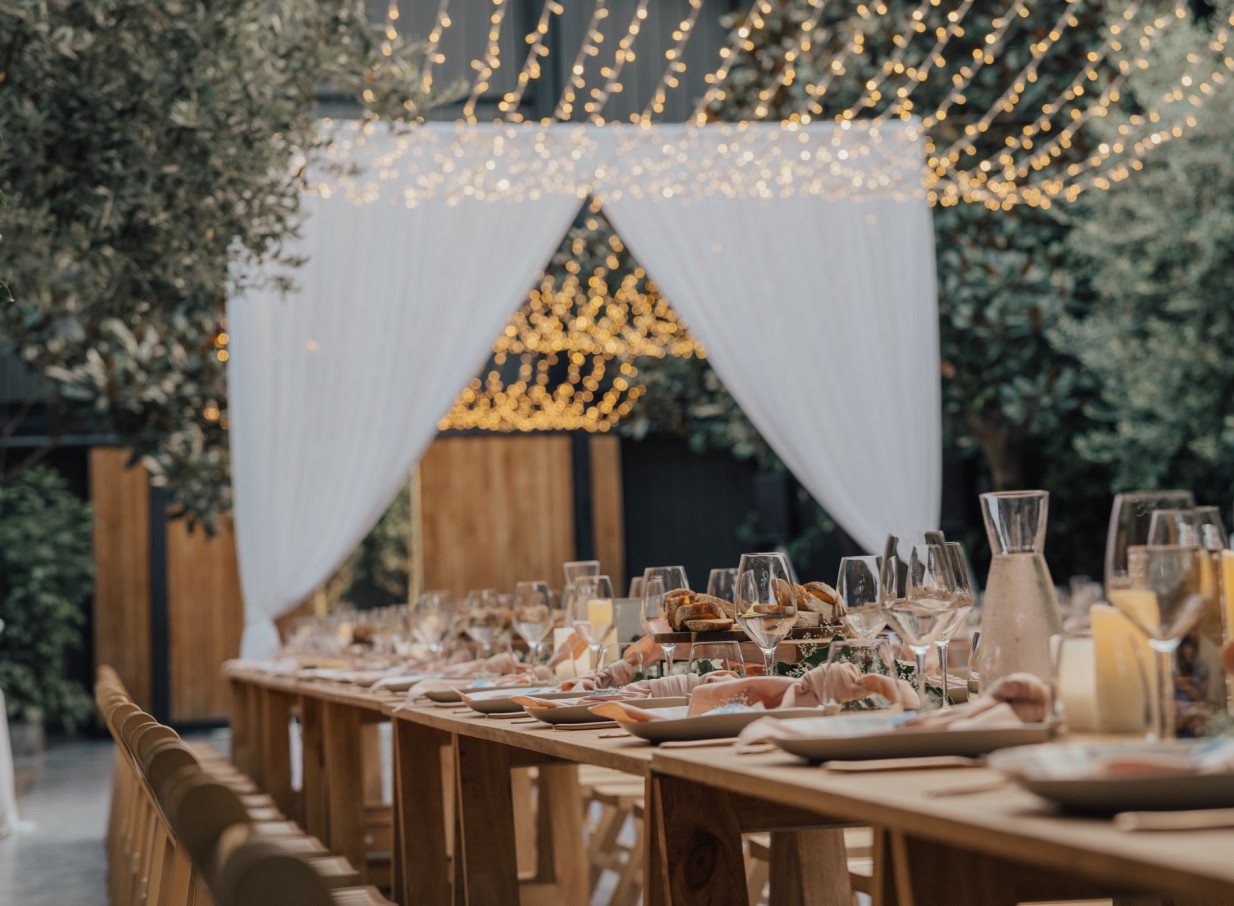 An elegant dining setup under fairy lights and white drapes within the glass-walled urban oasis of Glasshouse Morningside, Auckland.