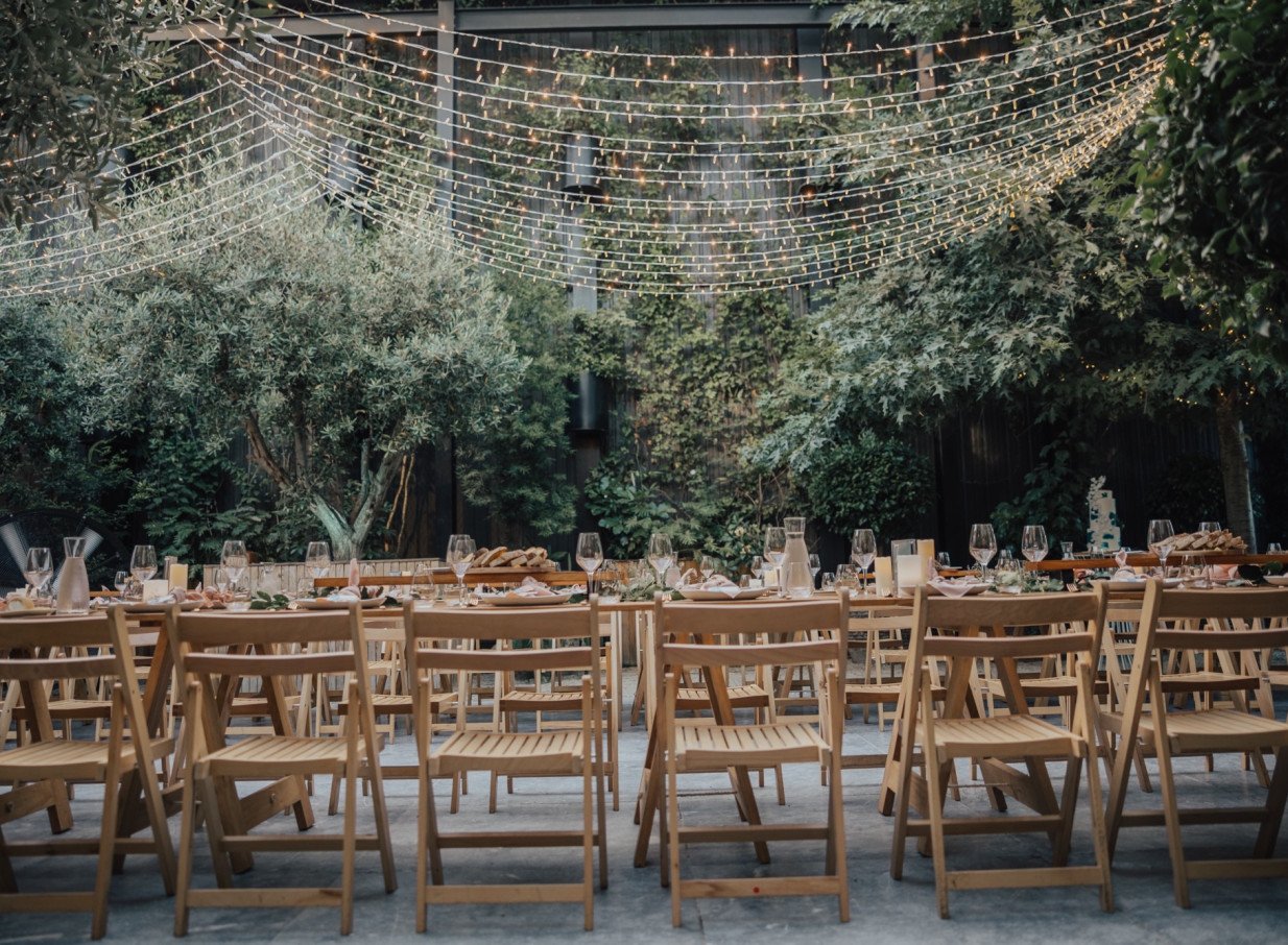 Outdoor dining under string lights amidst lush greenery at Glasshouse Morningside, Auckland, an industrial-chic urban oasis.