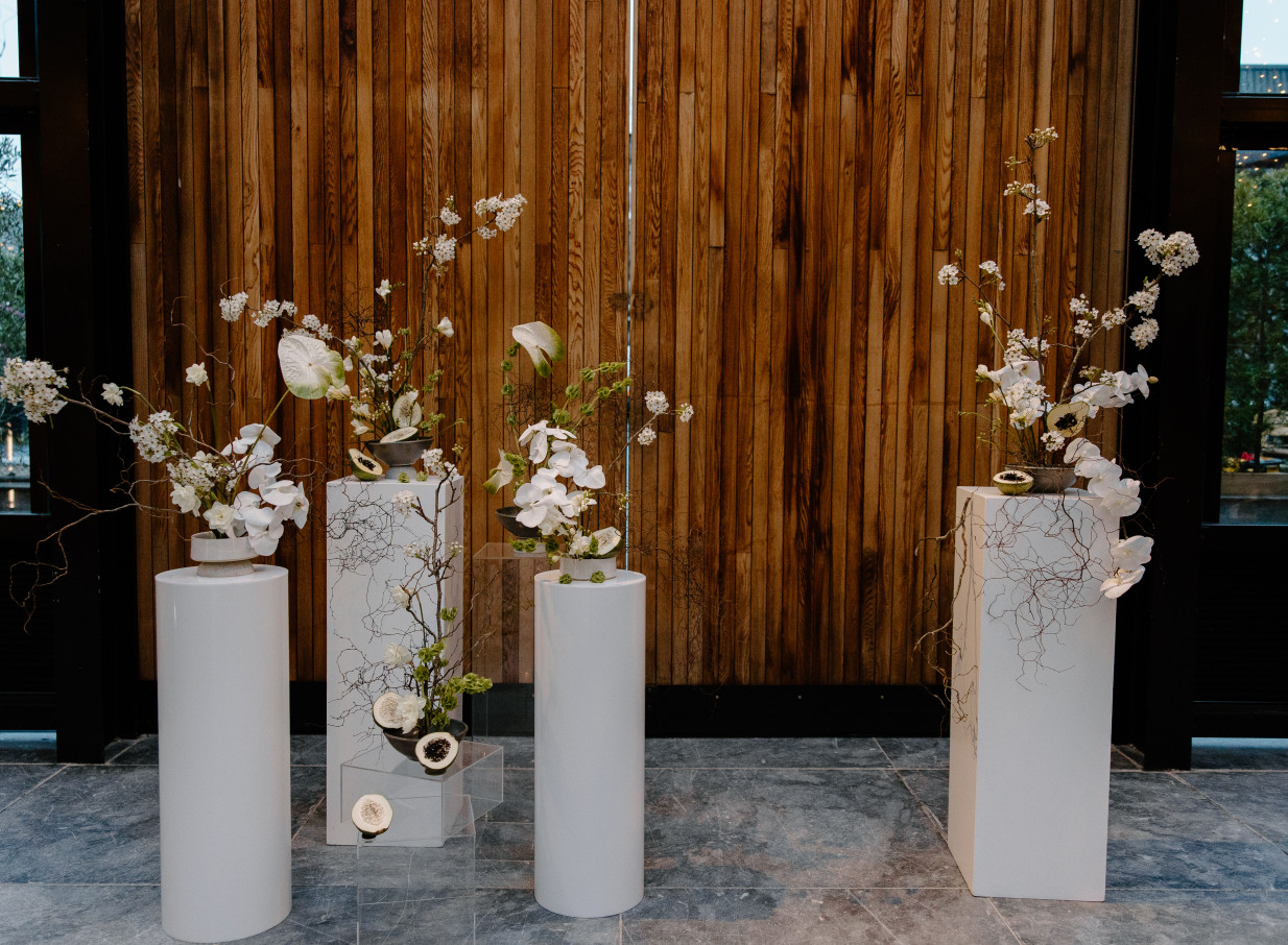 White floral arrangements on pedestals within the industrial-chic Glasshouse Morningside, Auckland.