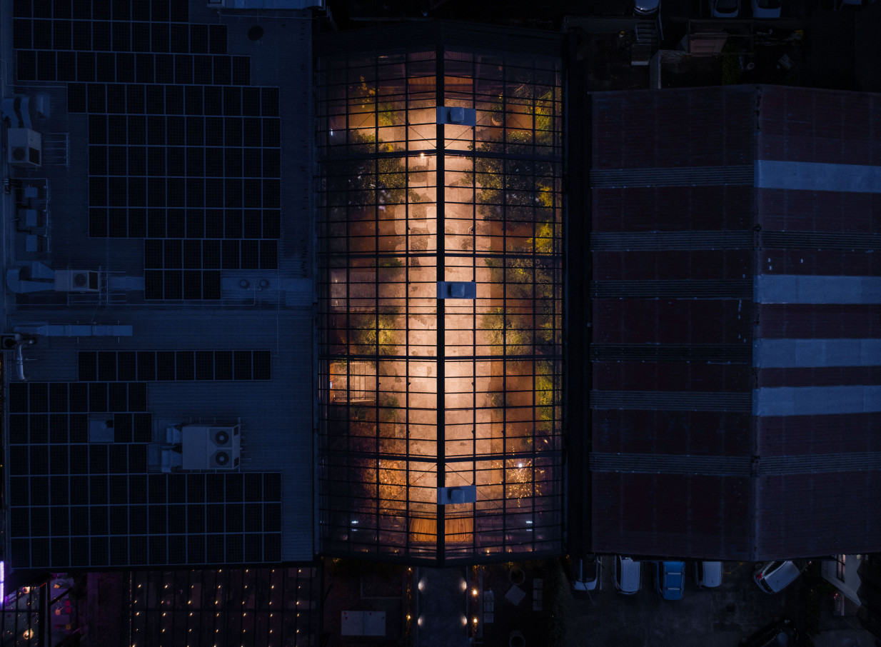 An aerial night view of Glasshouse Morningside, Auckland, revealing its illuminated glass-roofed event space with lush interior greenery.