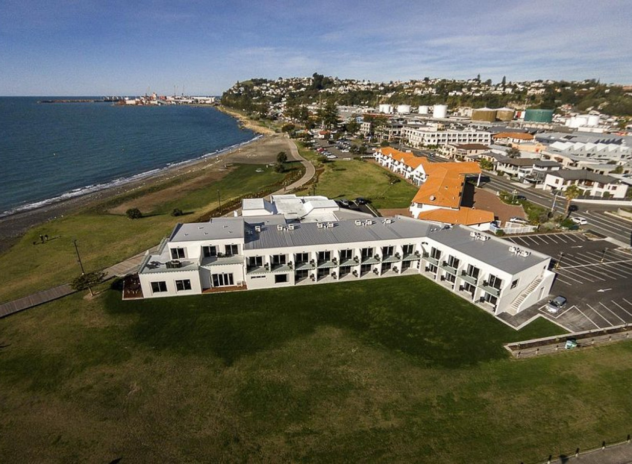 Aerial view of the modern East Pier Hotel in Hawke's Bay, a beachfront property with sea-facing balconies.