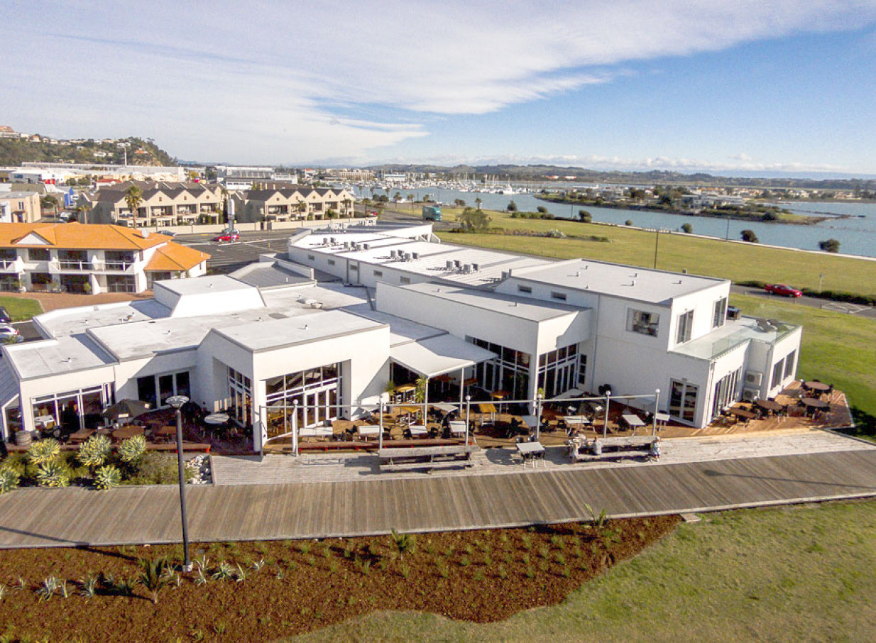 An aerial view of the modern East Pier Hotel in Hawke's Bay, featuring its waterfront brasserie and extensive outdoor decks.