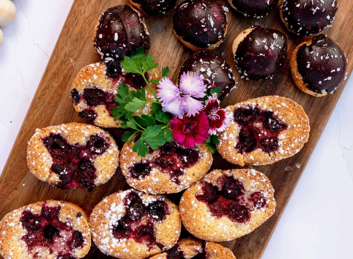 Fresh berry financiers and chocolate pastries on a wooden board, typical of Trinity Wharf Tauranga's refined waterfront dining.