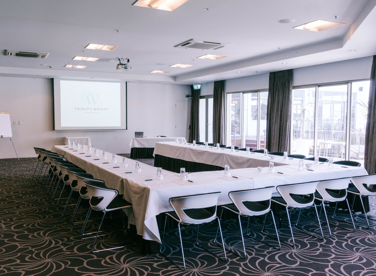 A coastal-inspired meeting room with a U-shaped setup and ample natural light at Trinity Wharf Tauranga.