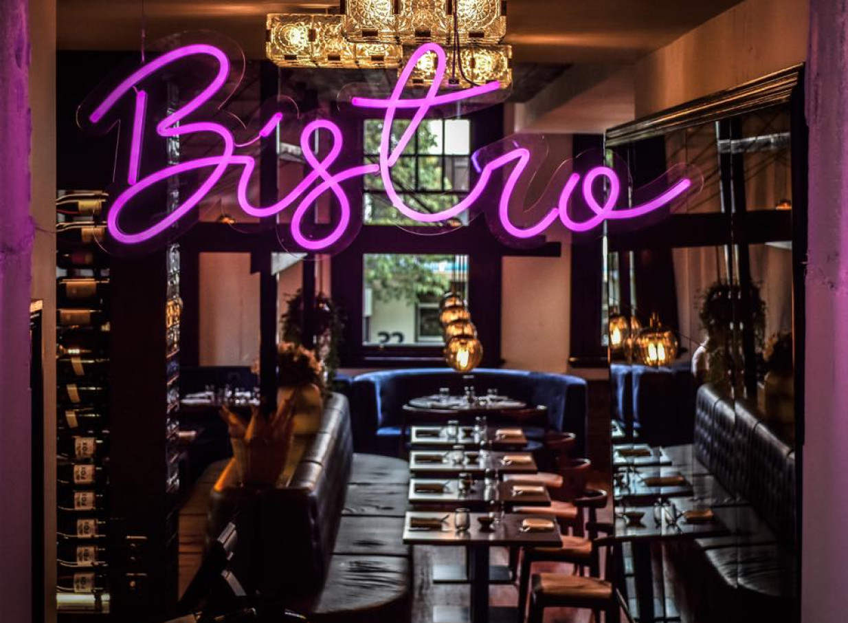 Pink neon 'Bistro' sign illuminates the elegant, modern dining area of Clarence Bistro in Tauranga's historic setting.