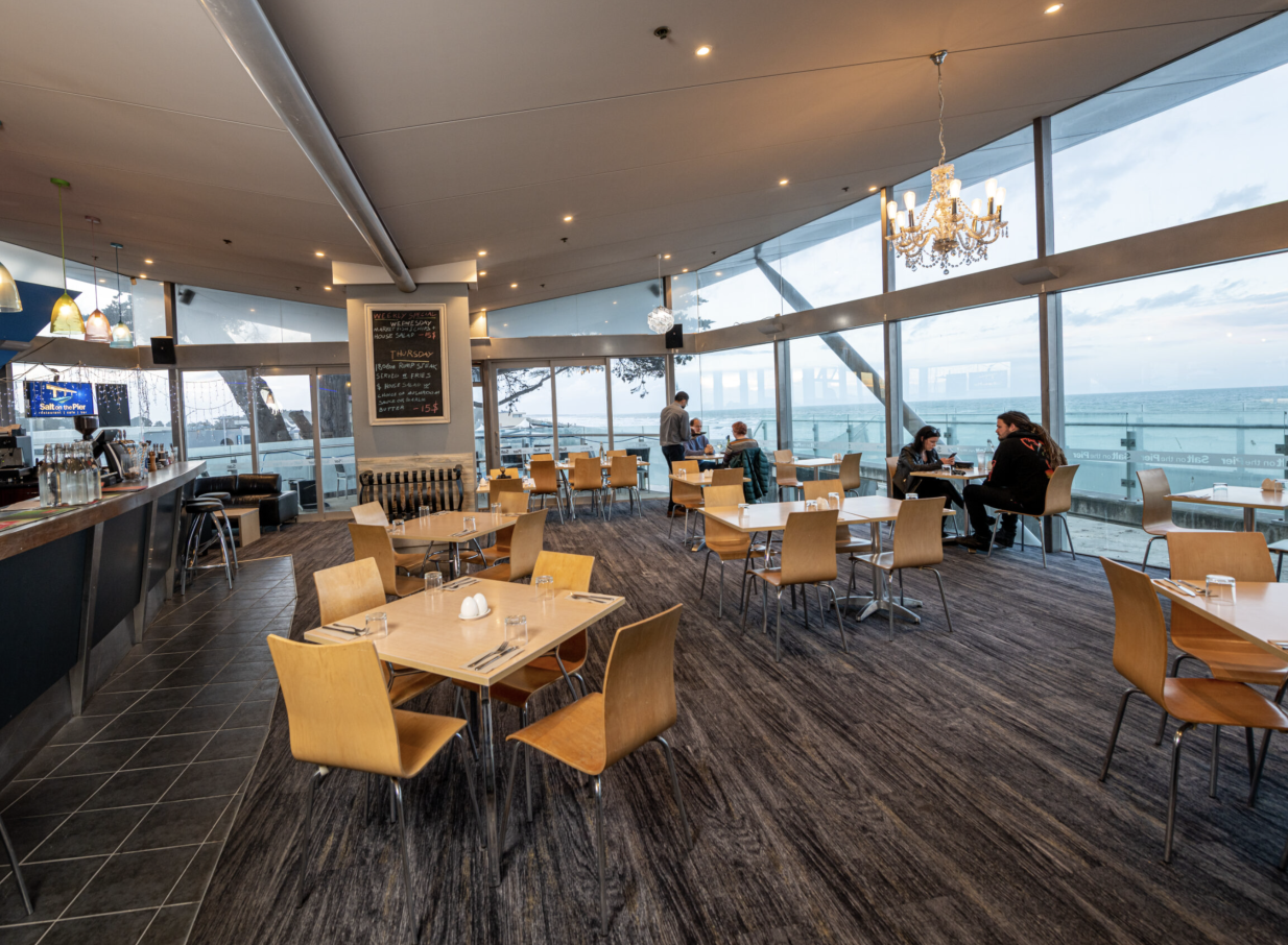The modern dining room of Salt on the Pier, Christchurch, features panoramic ocean views and contemporary decor.