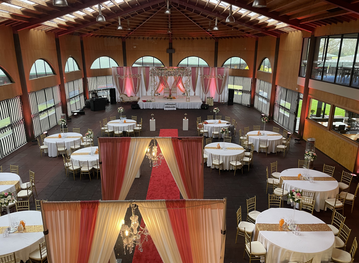 A spacious wedding reception at Karaka Pavilion in Auckland, a modern venue with high ceilings and large arched windows.