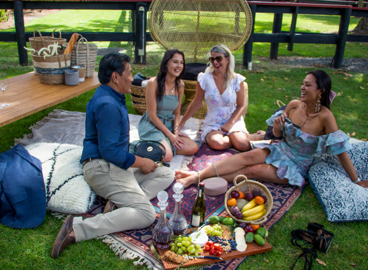 Friends enjoy an elegant outdoor picnic amidst the manicured gardens of Karaka Pavilion in Auckland.