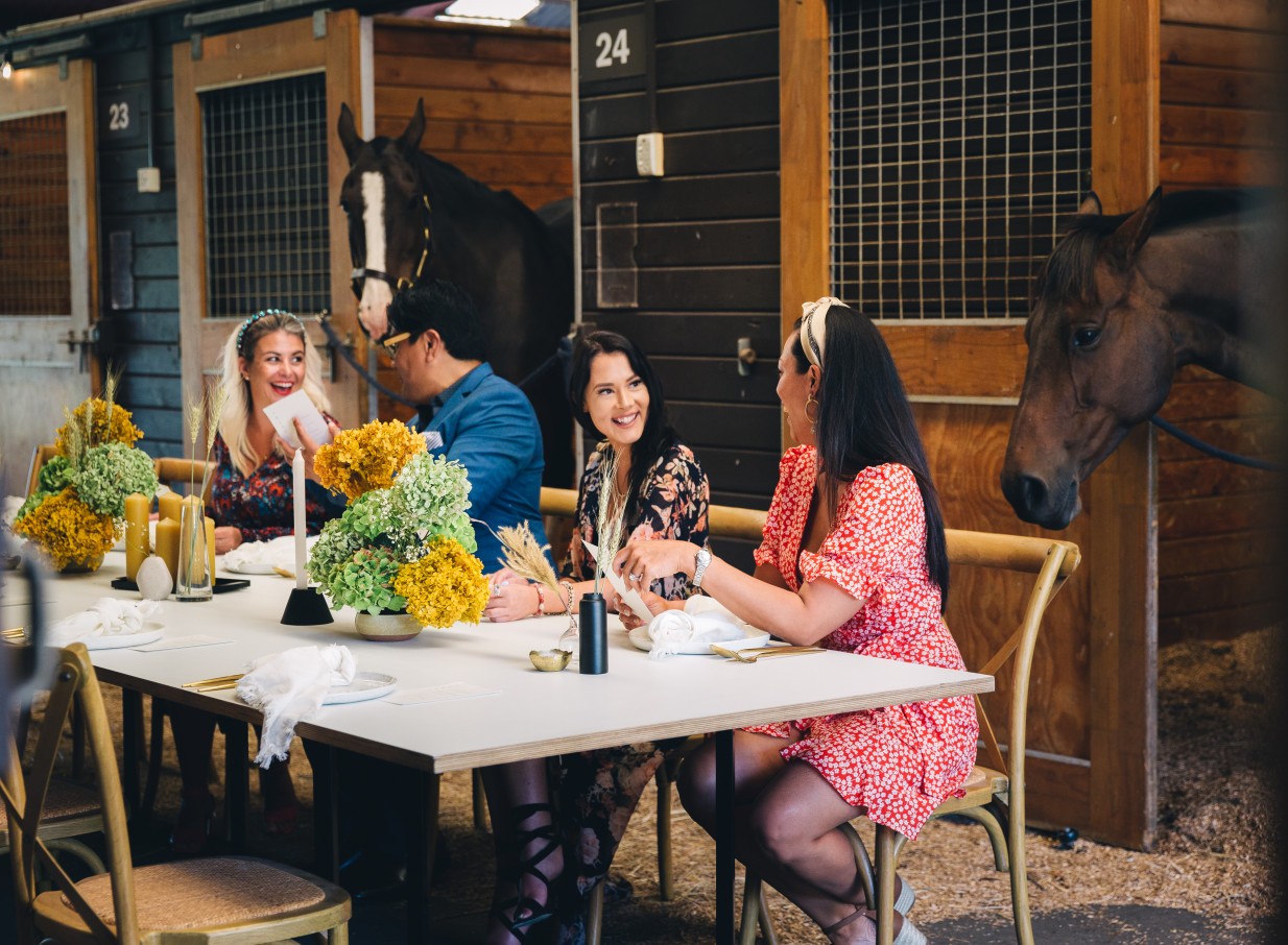 Guests enjoy dining at Karaka Pavilion, Auckland, within its unique stable setting, with horses visible in stalls.