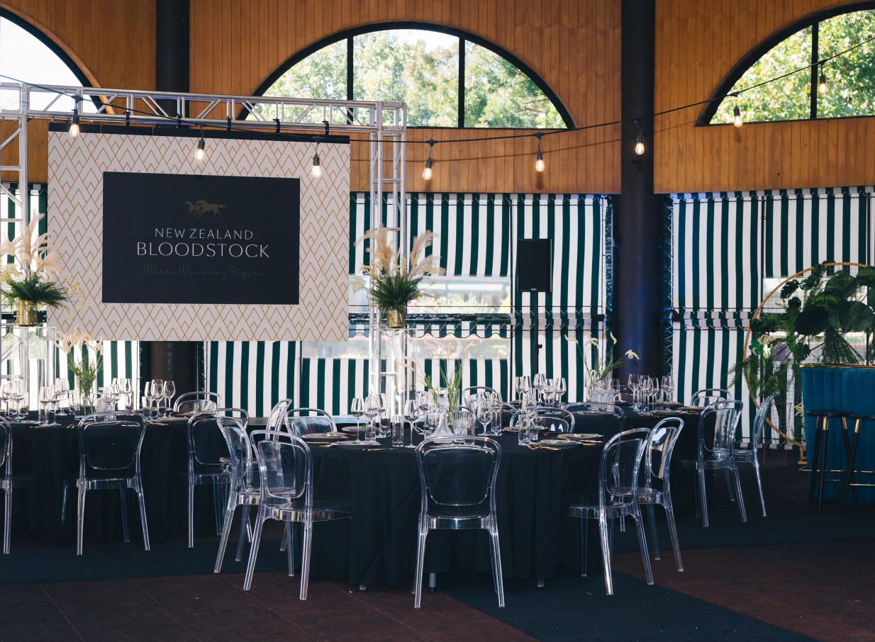 Karaka Pavilion, Auckland, presents a modern event space with high wooden ceilings, arched windows, and striped retractable awnings, set for dining.