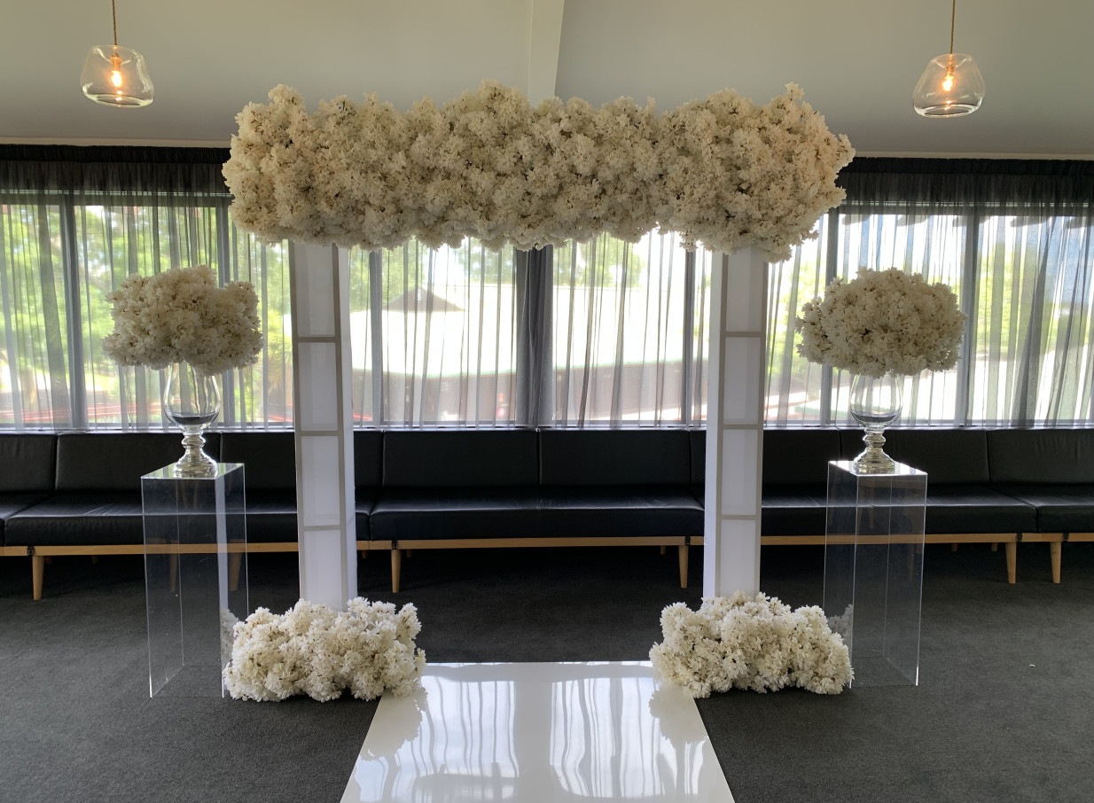 An elegant indoor wedding ceremony setup, featuring a white floral arch, at Karaka Pavilion in Auckland, showcases its versatile modern event space.