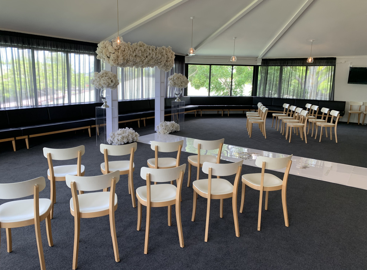 A modern ceremony setup with white floral decorations and an aisle in the spacious Karaka Pavilion, Auckland.