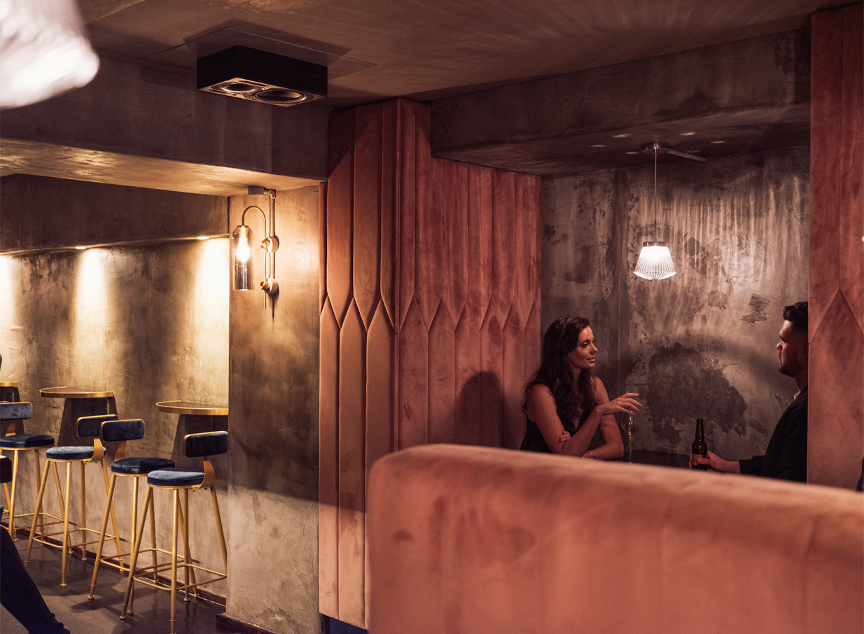 Thursday Bar Auckland's speakeasy-inspired setting, with a couple conversing in a plush, dimly lit booth.