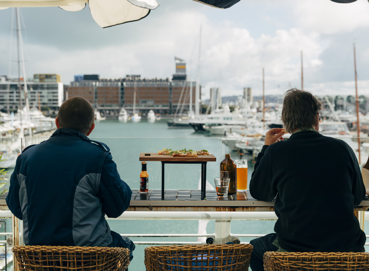 Two people enjoy drinks and food on the patio of Dr Rudi's, a vibrant Auckland rooftop bar overlooking the Viaduct Harbour.