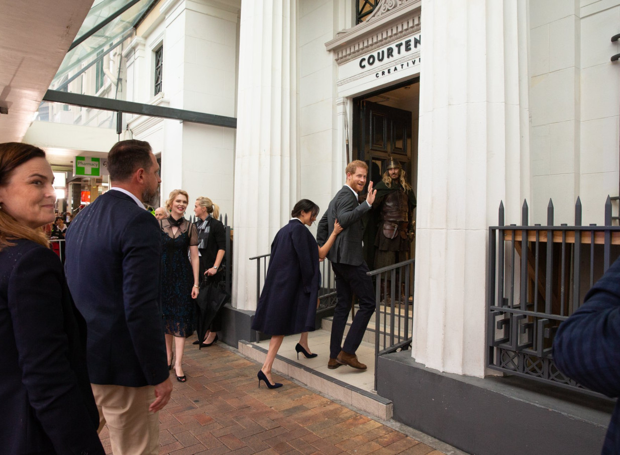 Prince Harry and Meghan Markle enter the grand, historic Courtenay Creative building in Wellington, with a costumed figure inside.