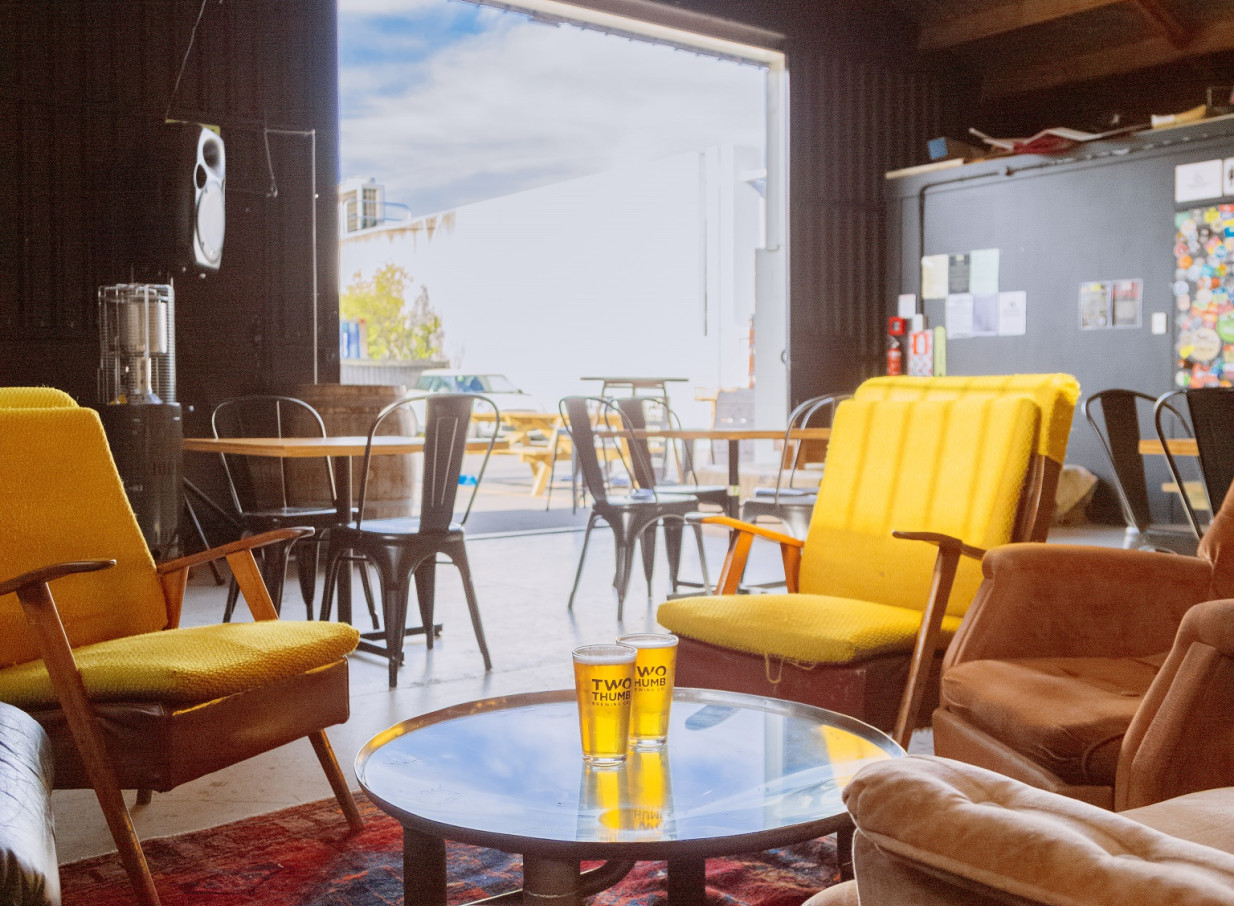 A laid-back, industrial-chic lounge at Two Thumb on Manchester, Christchurch, features mismatched seating and an open view to the outside.