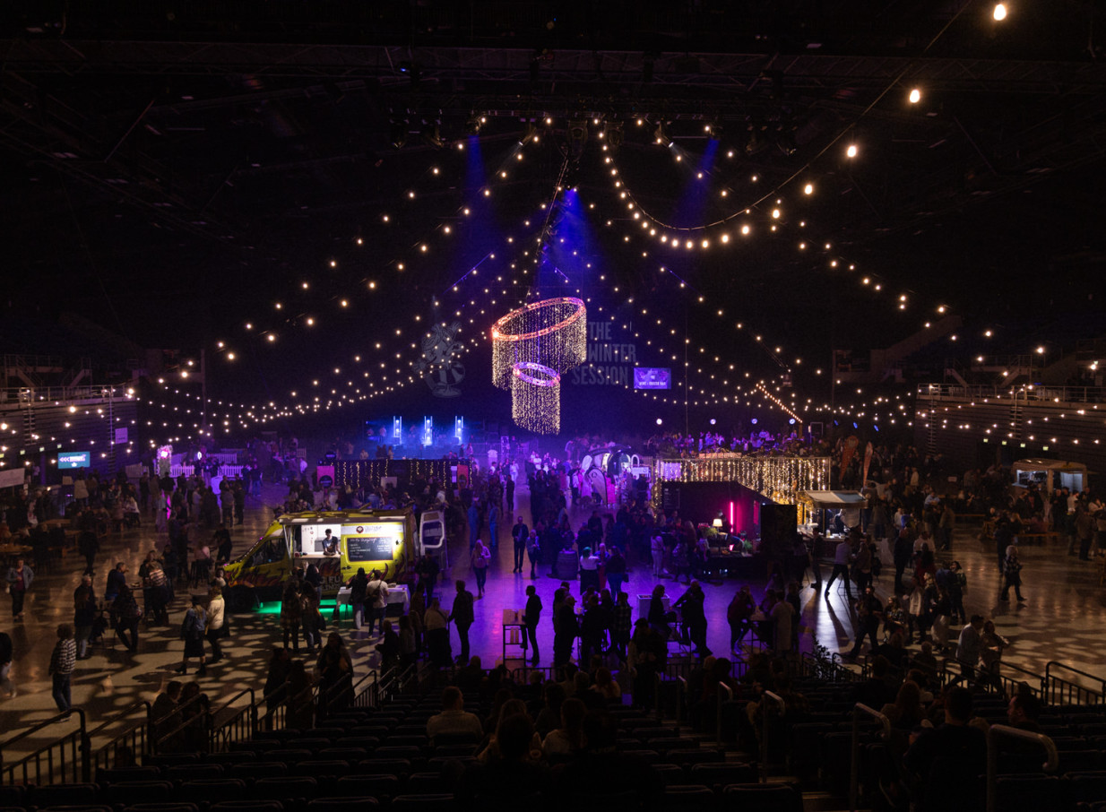 A festive indoor event at Christchurch's versatile Wolfbrook Arena, adorned with string lights, vendor booths, and a food truck.