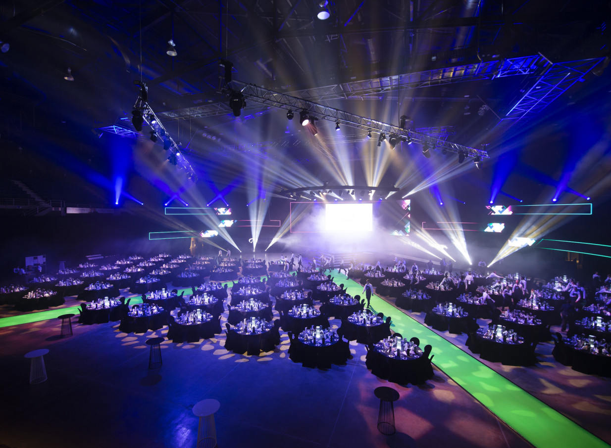 A vibrant gala dinner setup fills the adaptable Wolfbrook Arena in Christchurch, illuminated by dramatic blue and yellow event lighting.