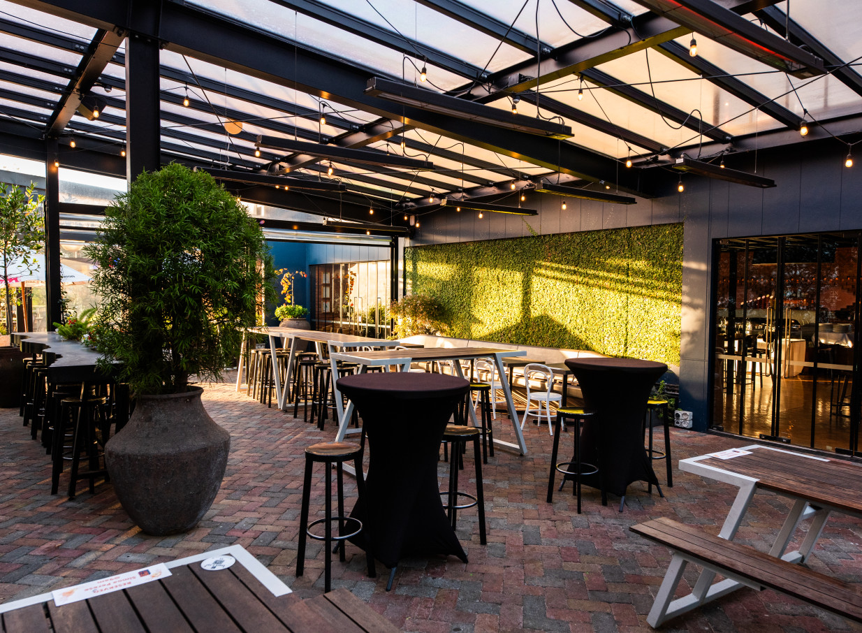 Morningside Tavern, Auckland, features a covered rustic industrial courtyard with high tables and a vibrant green wall.