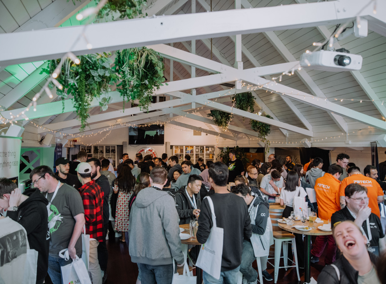 A lively gathering at Mission Bay Taproom in Auckland, featuring a high-pitched A-frame ceiling adorned with festive lights and greenery.