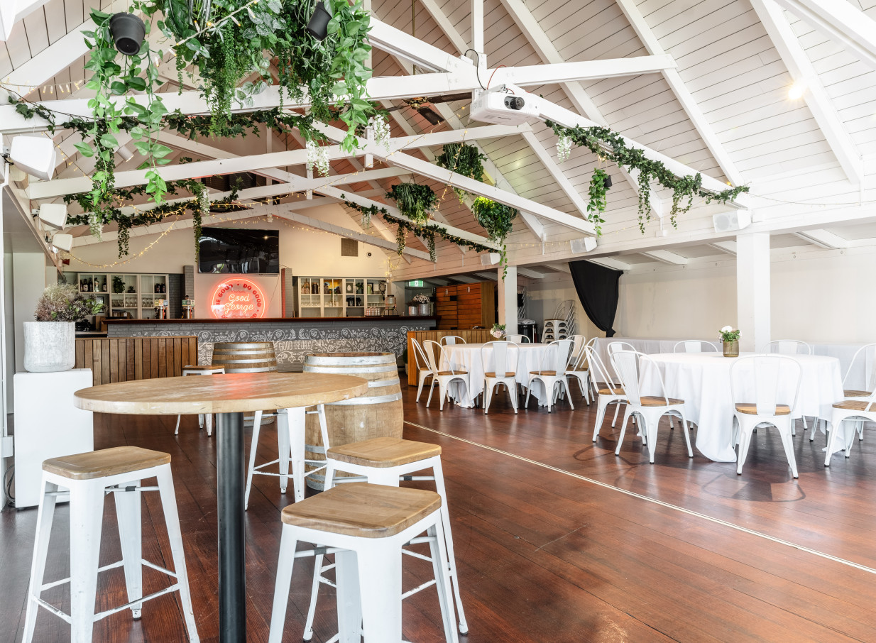 Mission Bay Taproom, Auckland, features a rustic-modern event space with a high-pitched ceiling, bar, mixed seating, and greenery.