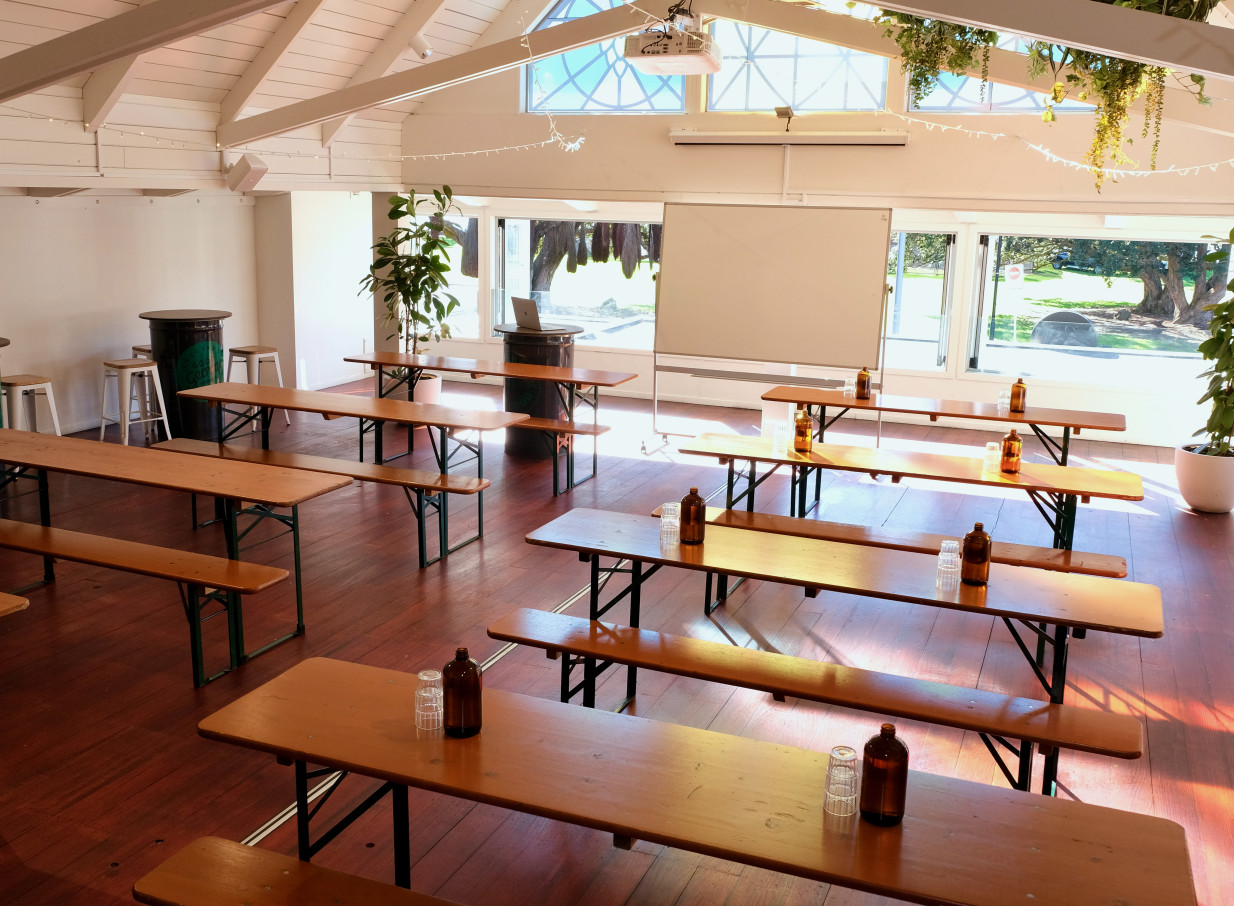 A bright, modern A-frame event room at Mission Bay Taproom in Auckland, featuring long wooden tables and benches.