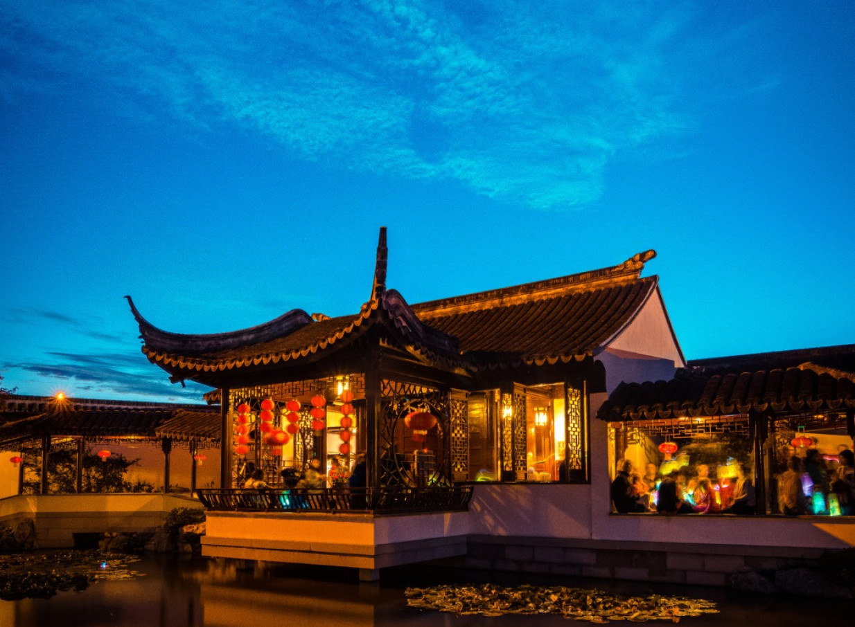 An illuminated traditional Chinese pavilion in Dunedin Chinese Garden, designed in authentic Jiangnan style, welcoming guests by the water.