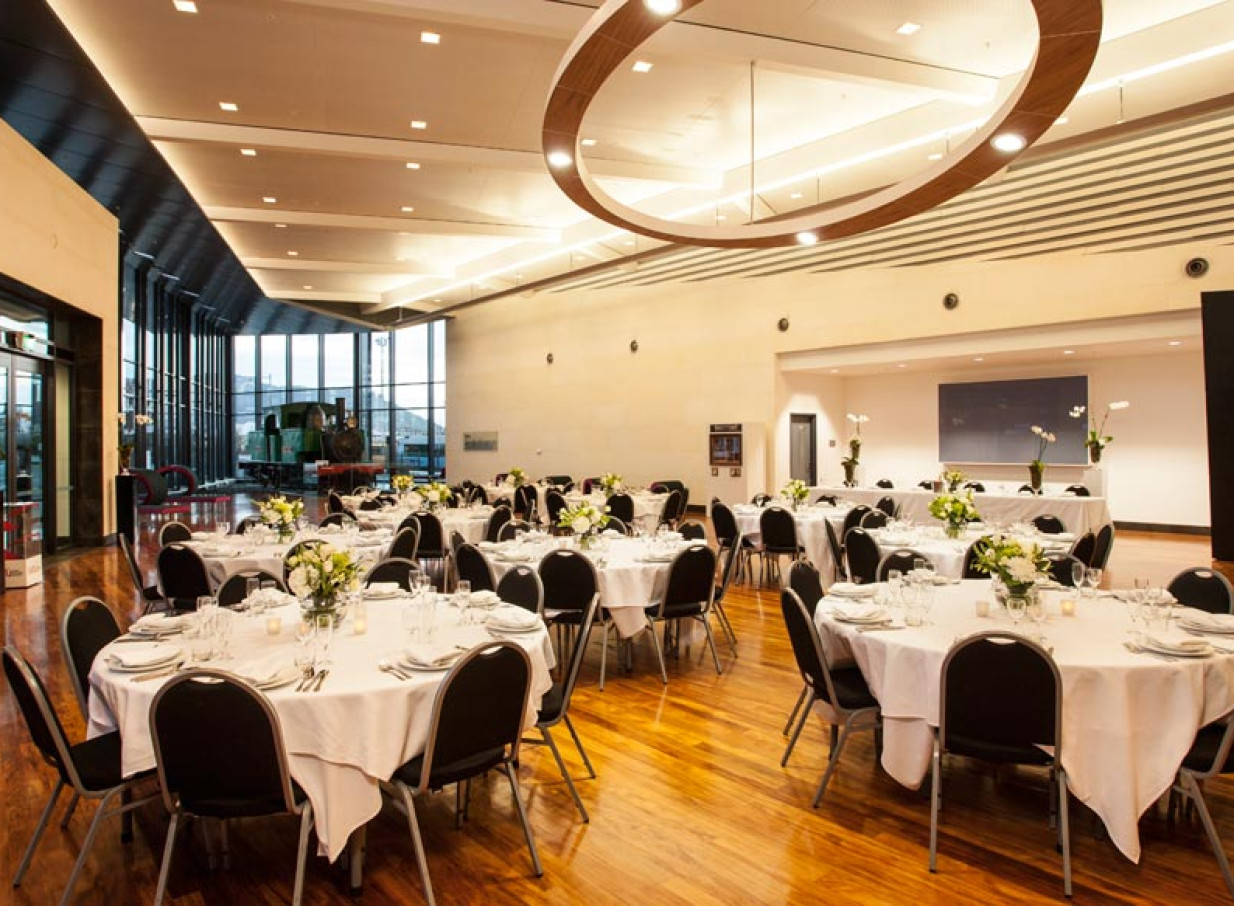 The Toitū Otago Settlers Museum's modern event space in Dunedin, set for a banquet, offers high ceilings, large windows, and a view of a historic train.